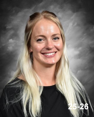 Portrait of a smiling woman with long, light blonde hair, wearing a black top, against a gray background.
