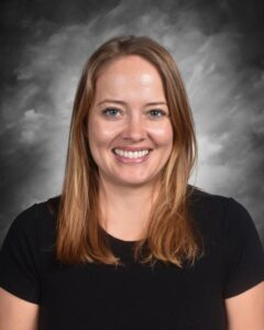 Smiling woman with long, straight hair wearing a black shirt, set against a gray background.