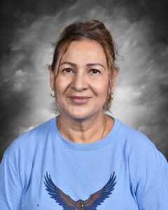 Smiling woman with long hair, wearing a blue shirt featuring an eagle design, against a gray background.
