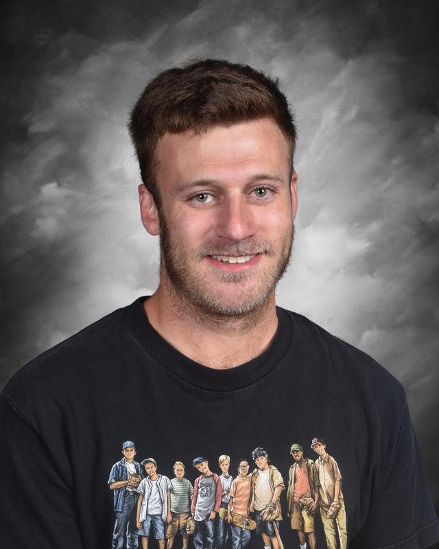 Smiling man with short hair wearing a black t-shirt featuring a group of boys, against a gray background.