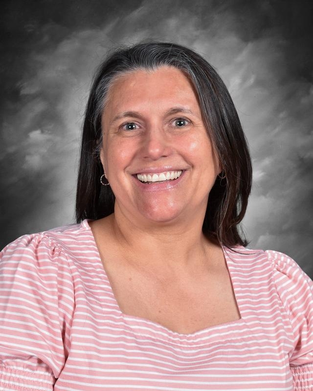 Smiling woman with long dark hair, wearing a pink striped shirt, against a gray background.