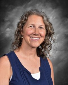 Woman with curly hair smiles, wearing a navy blue top against a gray background.