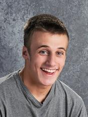 Smiling young man with short hair, wearing a gray shirt, set against a textured gray background.