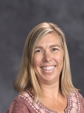 Smiling woman with shoulder-length blonde hair, wearing a maroon shirt, against a gray background.