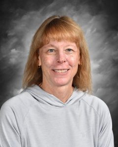 Woman with shoulder-length hair wearing a light gray hoodie, smiling against a gray, cloudy background.