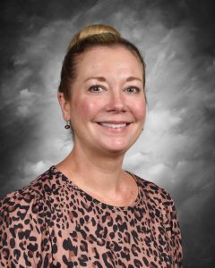 Smiling woman with hair in a bun, wearing a leopard print top, against a gray, cloudy background.