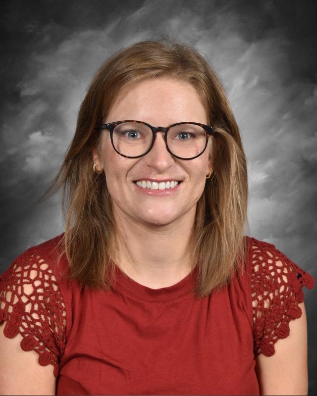 A person with glasses smiles, wearing a red top with lace sleeves, against a gray background.