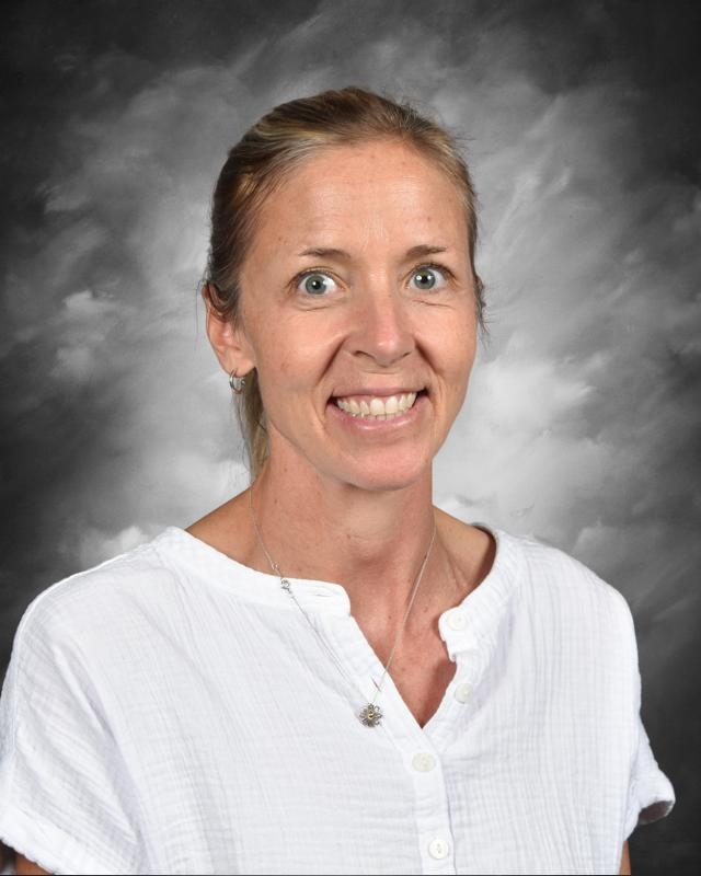 Smiling woman with light hair in a white shirt, set against a cloudy gray background.