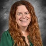 Smiling woman with long red hair, wearing a green blouse, against a gray background.